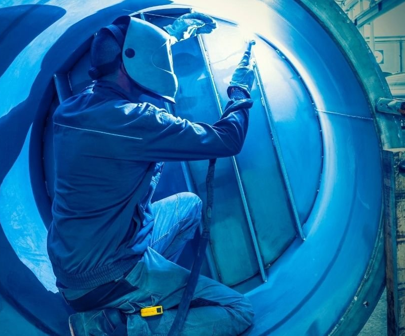 Industrial worker welding inside a large steel vessel